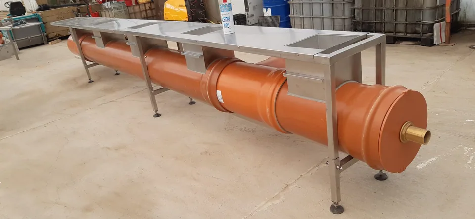 Complete screw conveyor with feed inlets, resting on the workbench in the workshop