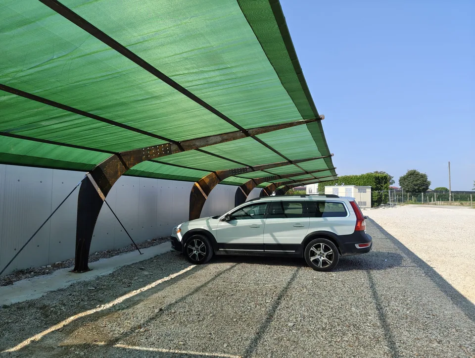 Tettoia in acciaio corten con telo ombreggiante verde, vista dal lato del posteggio